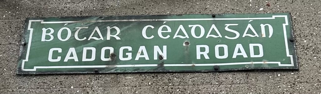 Photograph of street name plate for Cadogan Road, in Irish and in English, in white text on a green background.