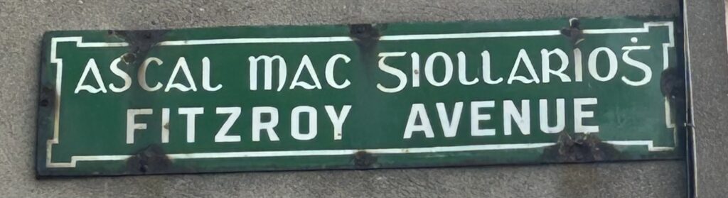 Photograph of street name plate for Fitzroy Avenue. The name is in Irish and in English, in white text on a green background.