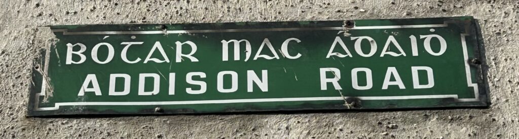 Photograph of street name plate for Addison Road, in Irish and in English, in white text on a green background.