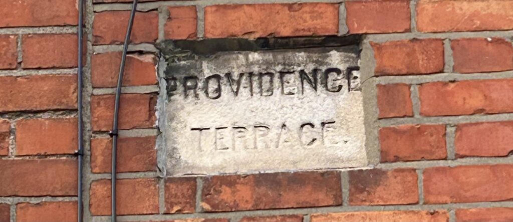 Photograph of street name plate for Providence Terrace. The text is engraved on a granite stone. affixed to the wall of a house.